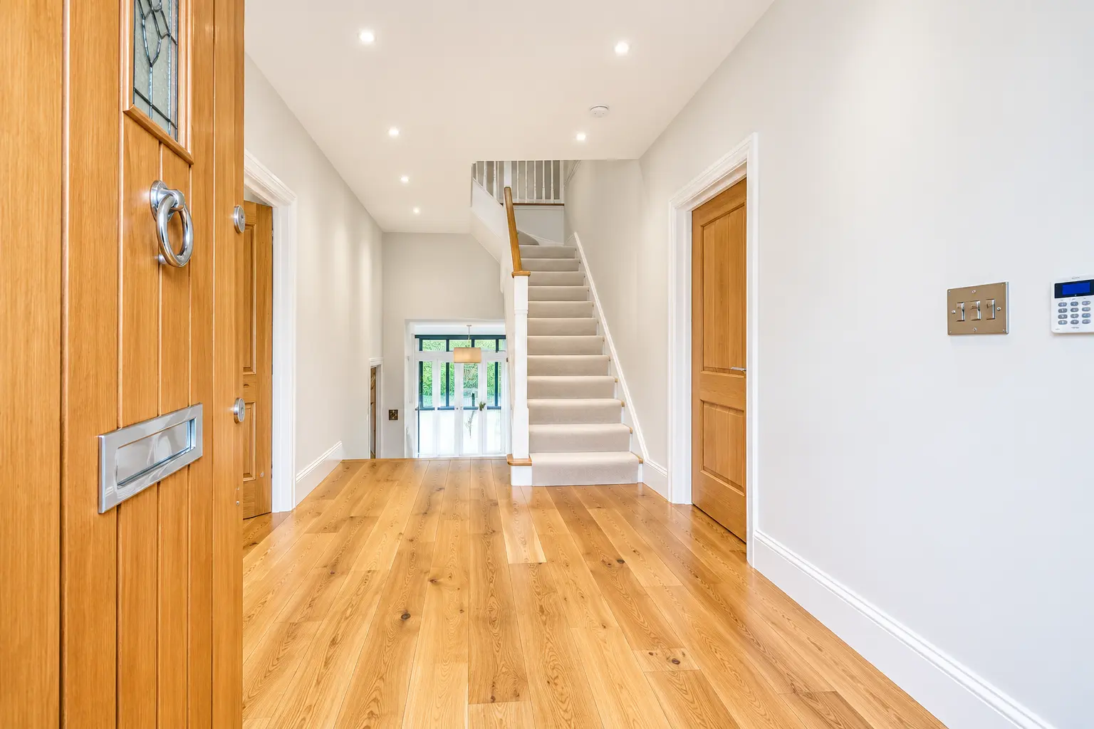 Bright hallway with oak flooring, oak doors and a carpeted staircase