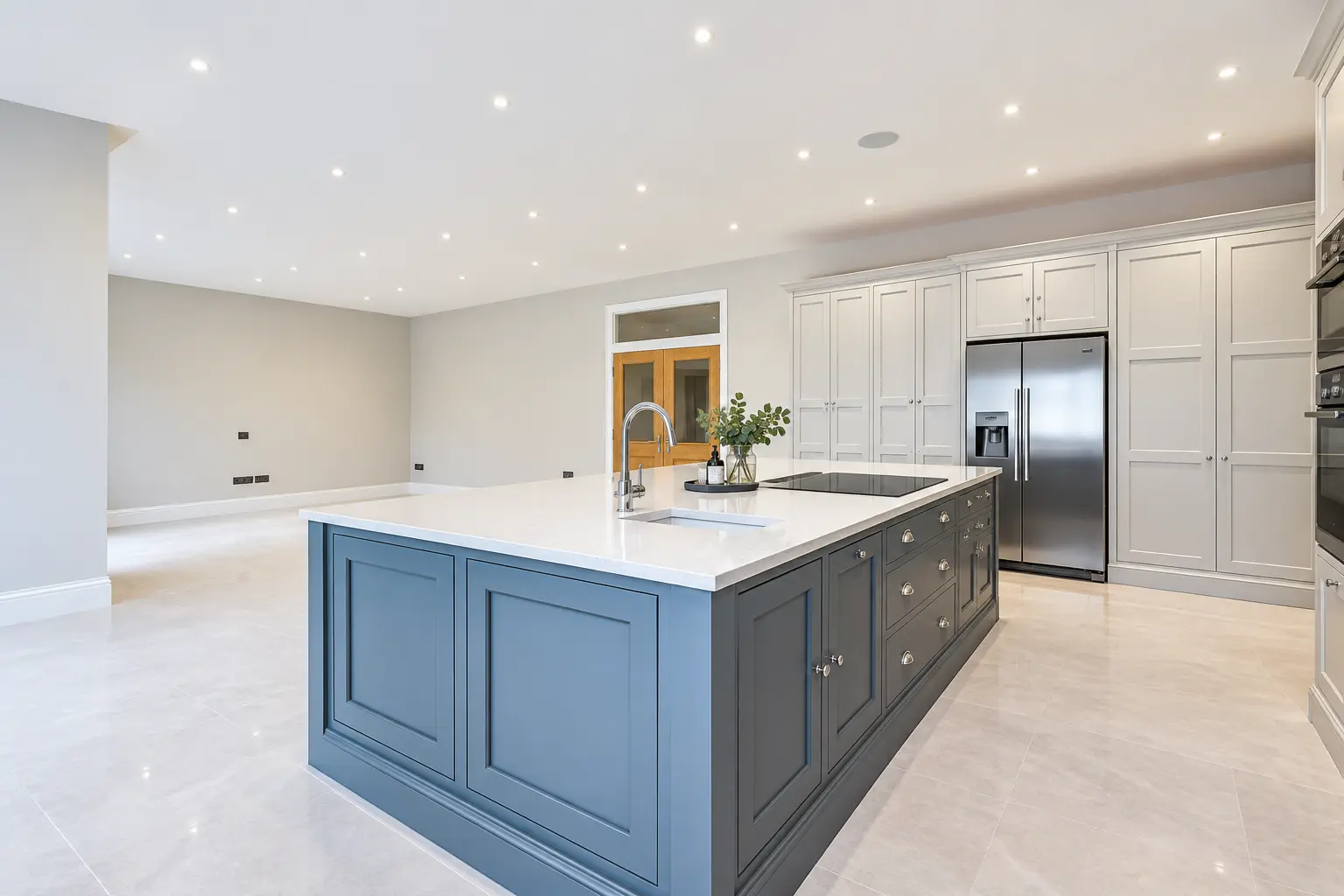 Large refurbished kitchen with blue island, white cabinetry and garden doors