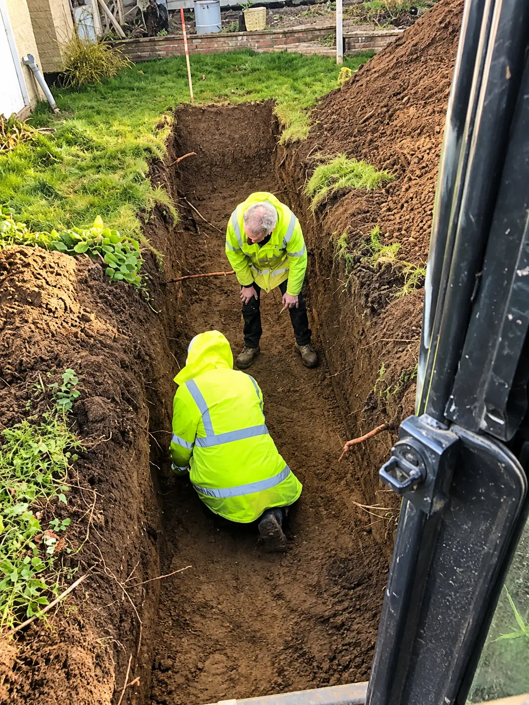 Two site operatives in high-visibility clothing working in a foundation trench